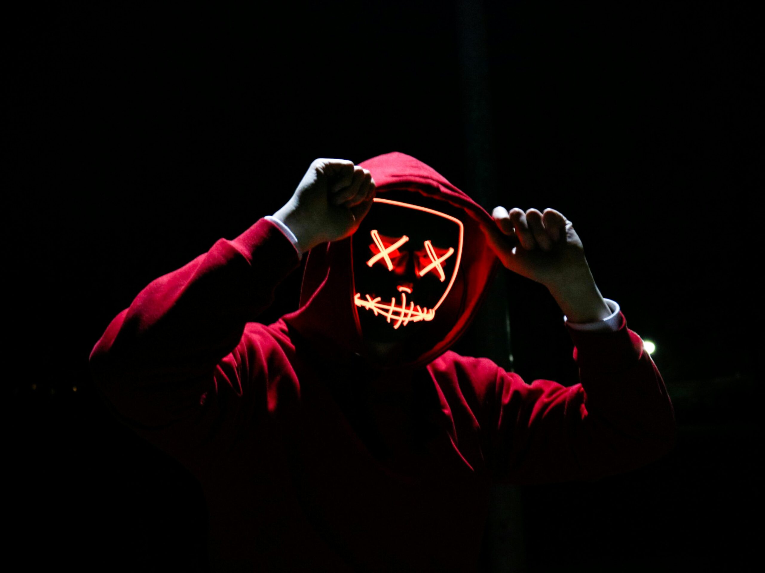pexels-photo-1097456-1097456 A spooky illuminated mask figure with a red hoodie in a dark setting, perfect for Halloween themes.